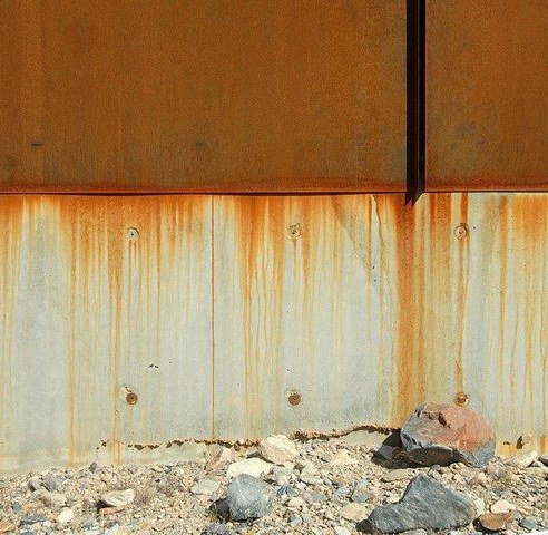 Corten steel panel over a board-formed concrete wall, with the bolts left exposed
