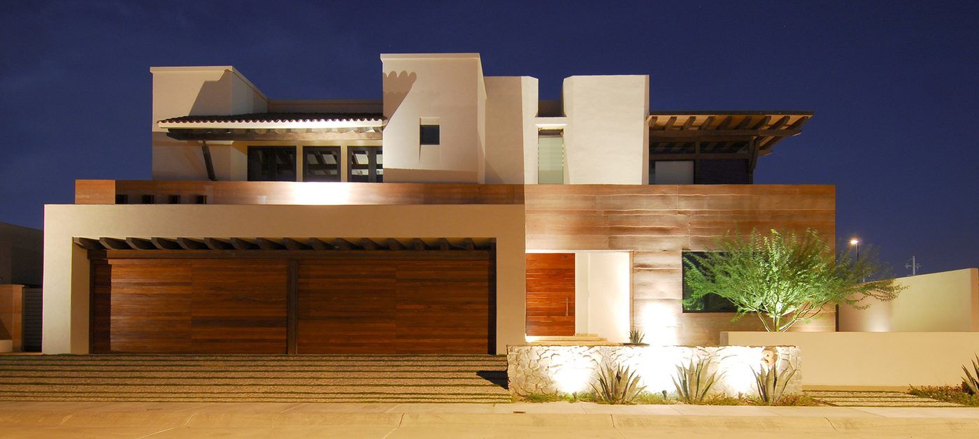 The house at dusk, lit from within, with the rammed-earth mass in shadow