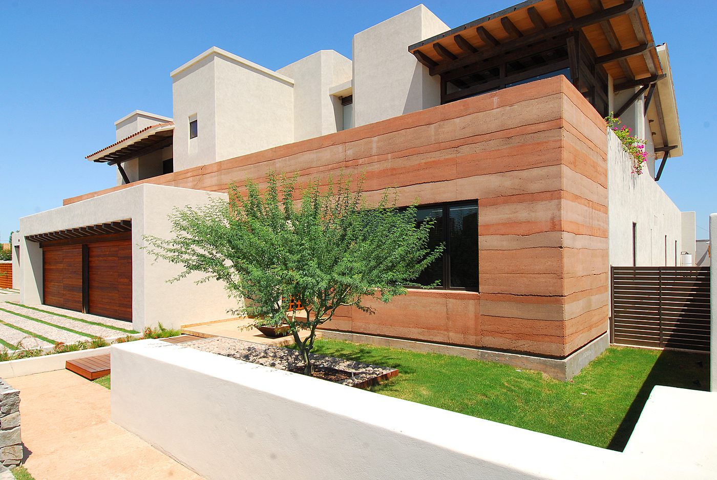 Living room with a full rammed-earth wall, a beamed timber ceiling and a sliding wall open to the garden