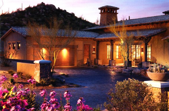 Motor court at dusk, with the entry lit, flowering planting in the foreground and the tile roofs beyond