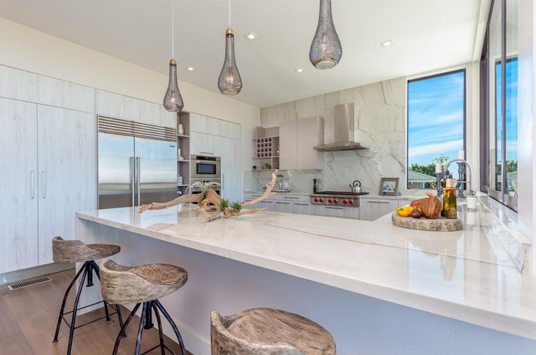 Kitchen with a marble island, pendant lights and a window wall onto the view