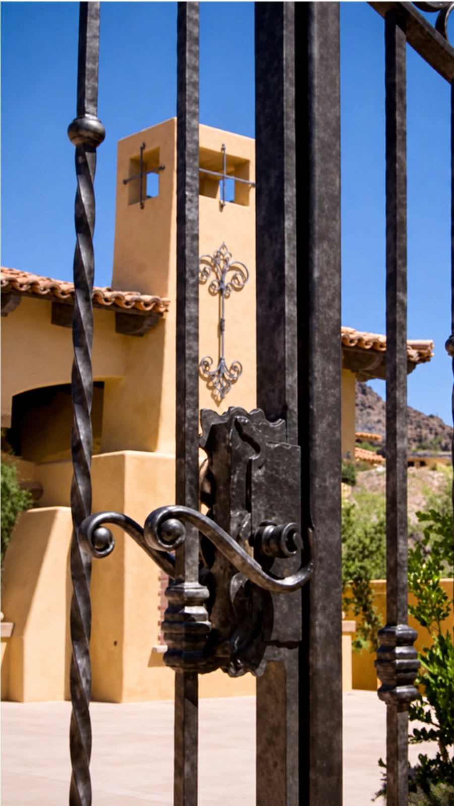 Wrought-iron gate with twisted bars, the adobe bell tower and its forged cross beyond